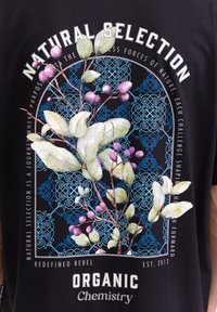 Schwarzes T-Shirt mit einer botanischen Illustration von grünen Blättern und lila Beeren. Kreisförmiges geometrisches blaues Muster mit Textelementen.