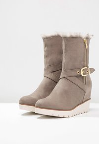 Grå kileboots med kunstpelsfor, lynlås lukning og justerbar remfunktion. Tekstureret overdel med gummisål.