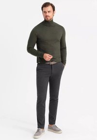 Pull à col roulé vert foncé, design ajusté, associé à un pantalon gris ajusté. Chaussures : baskets décontractées grises. Ceinture soignée visible.