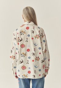 Kreemjas särk värviliste lille- ja linnumustritega. Omaduseks on voltkragen ja nööbitavad mansetid. Kandmiseks kombineeritud hele siniste teksadega.