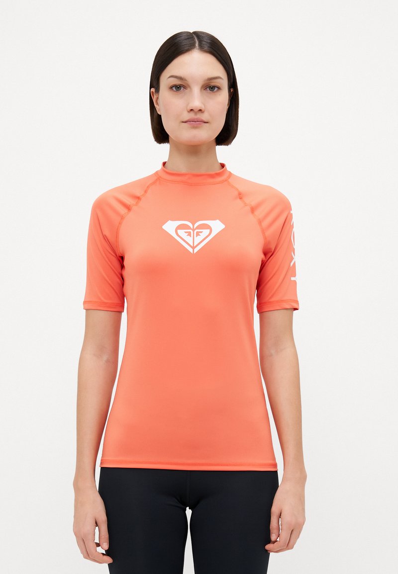 Kortermet, korallfarget rash guard med høy krage, som har en hvit hjerte-logo på brystet og tekstakenter på ermene. Glatt, elastisk materiale.