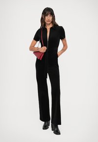 Mono negro de manga corta, con cremallera en la parte delantera y un cinturón en la cintura. Combinado con botas negras de tacón y un pequeño bolso rojo.