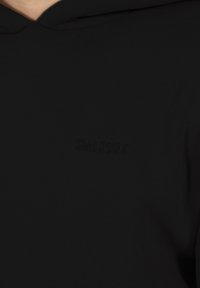 Sudadera negra con capucha, fabricada en un material suave y texturizado, con un logo en relieve "SMILODOX" en el pecho. Diseño sencillo con una forma clásica.