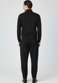 Chándal deportivo negro con cuello alto, puños ajustados y rayas laterales, confeccionado con tela suave; pantalones ajustados con pliegues.