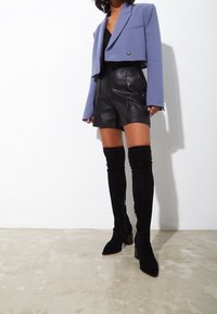 Blazer corto de color púrpura claro con un único botón redondo, combinado con shorts negros de cuero de tiro alto y botas negras de ante hasta la rodilla.