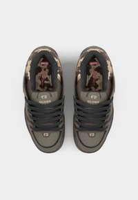 Green and brown sneakers with a textured finish, featuring a camouflage pattern and black laces. Logo embossed on the tongue and quarter.