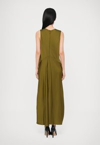 Olívazöld, ujjatlan maxiruha megkötött derékkal és légies, lefelé bővülő szoknyával; hátul cipzárral, letisztult, sima anyagtextúrával.