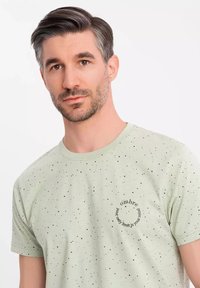 Camiseta verde claro con un patrón moteado, escote redondo y un pequeño gráfico que dice "tu única limitación es tu mente". Material de algodón.