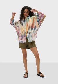 Multicolored button-up shirt with a flowing design, featuring a patterned texture in shades of orange, pink, blue, and cream. Paired with olive shorts.
