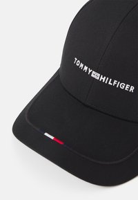 Sort baseball cap lavet af bomuld, med hvidt broderet "TOMMY HILFIGER" logo og små røde, hvide og blå detaljer på siden.