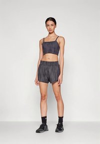 Conjunto desportivo cinzento escuro composto por um top cropped canelado com alças finas e calções largos com cintura elástica, feito de um material leve.