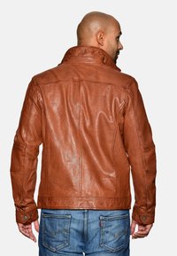 Bruine leren jas met een gestructureerde kraag, een tekstuurafwerking en zichtbare stikseldetails, gecombineerd met blauwe denim jeans.