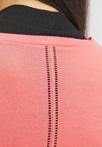 Tröja med en texturerad korallfärgad tyga med en kontrasterande svart ribbad krage och ett dekorativt vertikalt utskärningsdetalj längs sömmen.