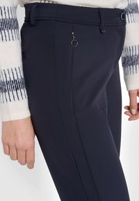 Pantaloni blu navy caratterizzati da una texture liscia, vestibilità slim e un piccolo zip tondo sul davanti. Dettagliati con passanti per cintura e cuciture laterali.