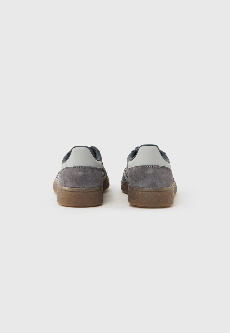 Gray suede sneakers with a smooth gray heel, rubberized gray accents, and a gum sole, showcased from the back on a white background.