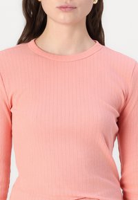 Top a maniche lunghe in morbido tessuto a coste di colore rosa chiaro, con scollatura rotonda. La texture è sottile con coste verticali su tutto il capo.