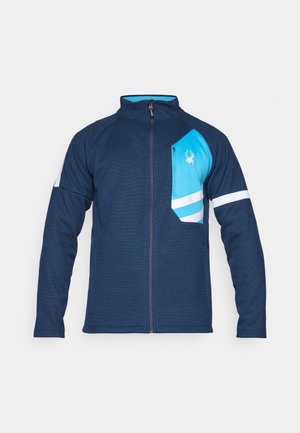Navy blue zip-up jacket with a textured finish, featuring a light blue chest pocket, white stripes on sleeves, and a small logo detail.