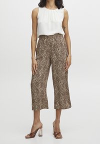 Spodnie w leopardzi wzór o szerokich nogawkach z elastycznym pasem, uzupełnione białą bezrękawną bluzką. Strój zawiera przezroczyste sandały na obcasie.