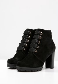 Bottines en suède noir avec une finition texturée, dotées de lacets en satin, d'œillets dorés et d'un talon épais pour plus de stabilité. Semelle épaisse pour une meilleure traction.