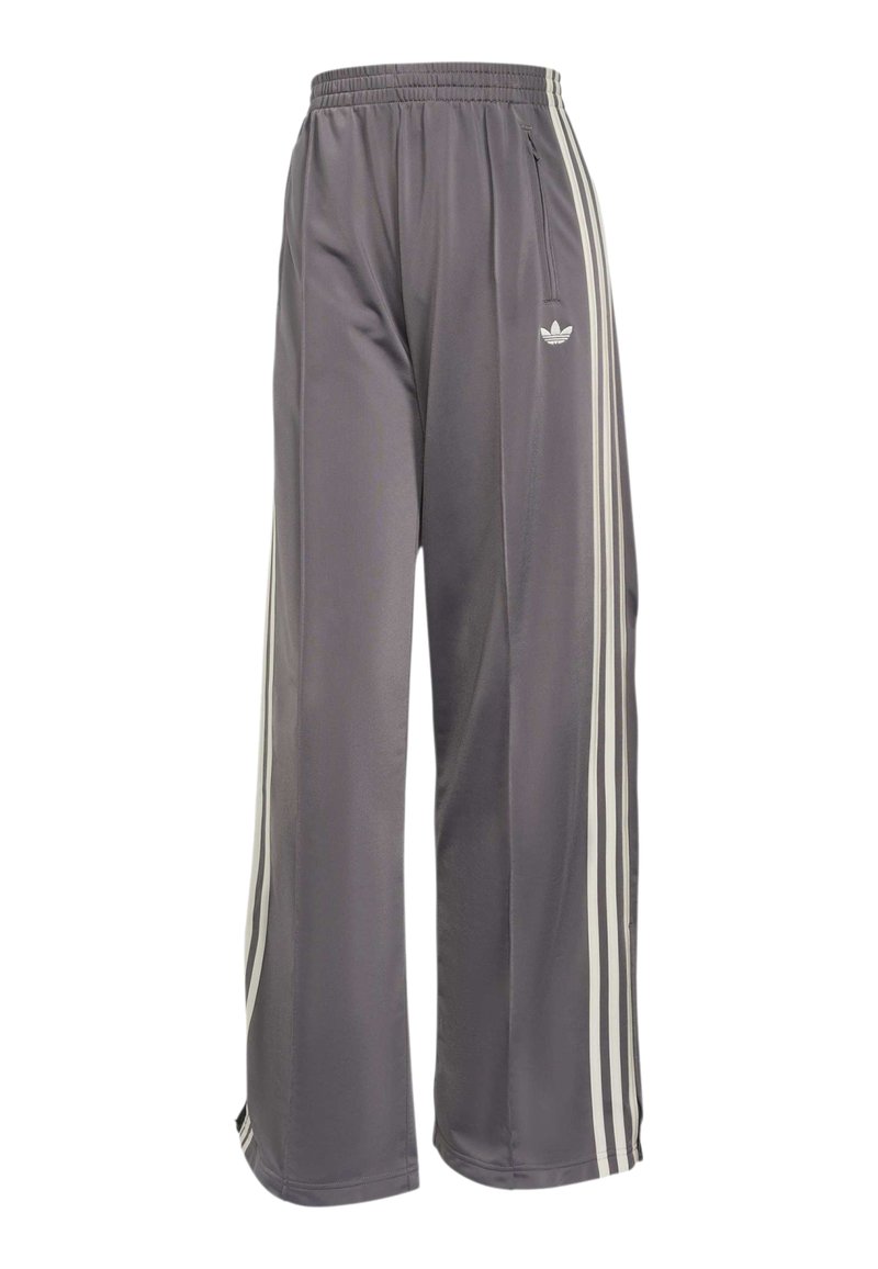 Pantalon de survêtement gris à jambes larges avec taille élastique, bandes blanches sur les côtés, poche zippée et logo Adidas sur la cuisse droite.