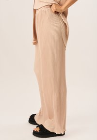 Pale pink, pleated wide-leg pants with an elastic waistband, featuring textured fabric and a flowy silhouette, paired with black sandals.