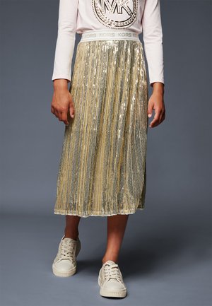 Jupe midi plissée dorée avec une texture en sequins scintillants et une taille élastique, associée à des baskets de couleur claire.