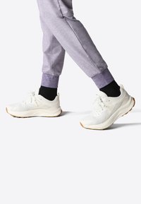 Scarpe da ginnastica bianche con sovrapposizioni in rete e sintetico, superfici testurizzate e suole in gomma, abbinate a joggers grigi con polsini a costine.