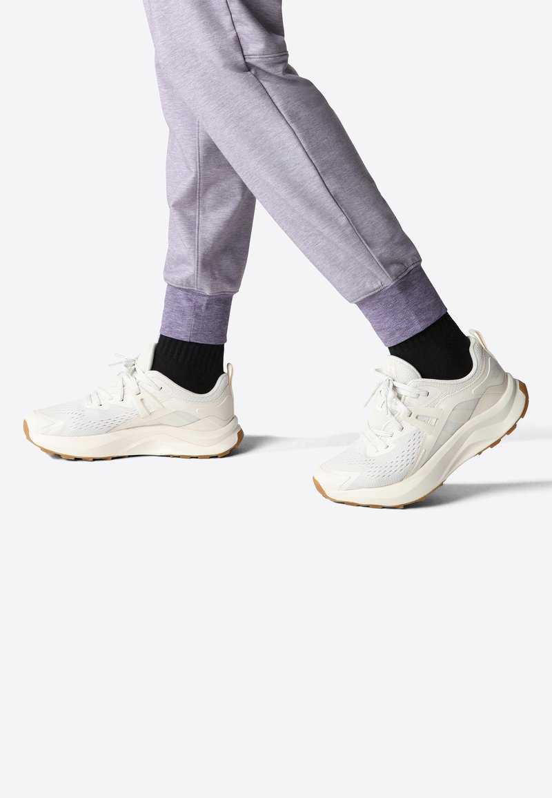 Scarpe da ginnastica bianche con sovrapposizioni in rete e sintetico, superfici testurizzate e suole in gomma, abbinate a joggers grigi con polsini a costine.