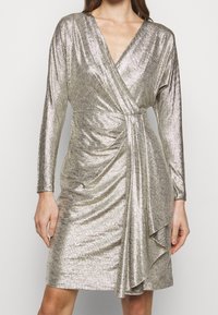 Metallic gold wrap dress with long sleeves, V-neckline, draped detail at waist, and smooth, textured fabric. Short length.