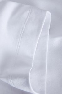 Weißer Stoff mit glatter Textur, der ein gefaltetes Bündchen und sichtbare Nähte entlang des Randes aufweist. Sauberes und minimalistisches Design.