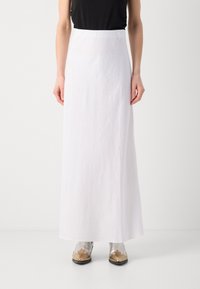 Long white skirt made of lightweight fabric, featuring a smooth texture and high waistband, paired with metallic shoes.