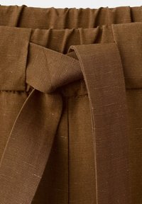Gros plan sur un pantalon en tissu marron avec une ceinture élastique à la taille et une ceinture en tissu nouée à l'avant.