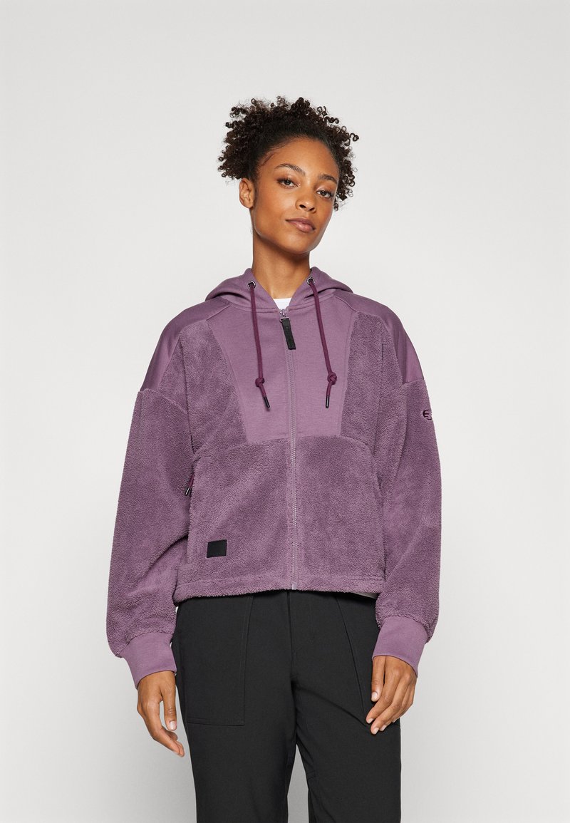 Veste en polaire violette avec capuche, dotée d'une fermeture éclair, de panneaux en tissu texturé et de poignets élastiques. Les accents noirs incluent un patch logo.