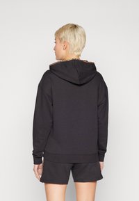 Sweat à capuche noir avec doublure en imprimé léopard à l'intérieur de la capuche, coupe oversized, texture douce, associé à des shorts noirs pour un look coordonné.