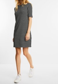 Randig klänning i svart och vitt med korta ärmar, rak skärning och sidofickor. Matchad med vita sneakers för en avslappnad look.