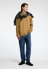 Ruda ilga rankovėm marškiniai, mėlyni džinsai ir juodi batai; žalia raštuota šalikas permestas ant pečių; glotni medžiaga ir laisvas siluetas.