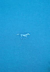 Světle modrá pánská polo košile s texturovanou látkou, na levé straně má malé vyšívané logo koně v tmavším modrém odstínu.