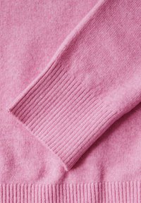 Section de pull léger rose avec des poignets côtelés et une texture lisse. Détails de couture visibles le long du bord. Convient pour une tenue décontractée.