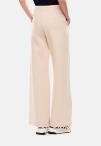 Pantalones de pierna ancha beige con una textura suave, que cuentan con bolsillos laterales y una cinturilla limpia, combinados con zapatillas blancas.