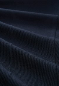 Marineblauwe textuurstof met een geribd patroon, met geplooide lagen. Het oppervlak is glad en gelijkmatig geweven, wat diepte en dimensie creëert.