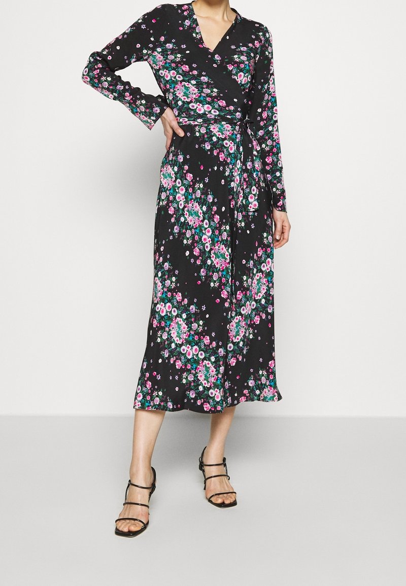 Schwarzes Wickelkleid mit langen Ärmeln und einem floralen Muster in Pink, Grün und Lila. Der Stoff ist weich und hat eine fließende Silhouette.