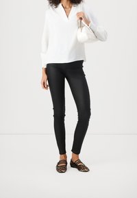 Blouse blanche à col en V, pantalon noir ajusté, et ballerines à motif animalier avec des brides ; portant un petit sac à main blanc.