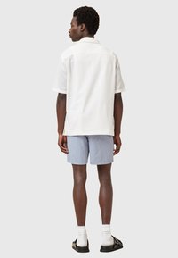 Camicetta bianca a maniche corte con un motivo testurizzato, abbinata a pantaloni corti azzurri chiari. L'outfit presenta una vestibilità rilassata e un design semplice.
