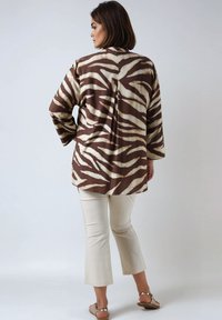Brown and cream zebra-striped blouse with wide sleeves, paired with light beige cropped pants and metallic sandals.