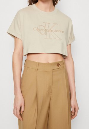 Beżowy krótki t-shirt z logo Calvin Klein Jeans w połączeniu z wysokim stanem i szerokimi nogawkami w kolorze jasnobrązowym, zapinany na guziki.