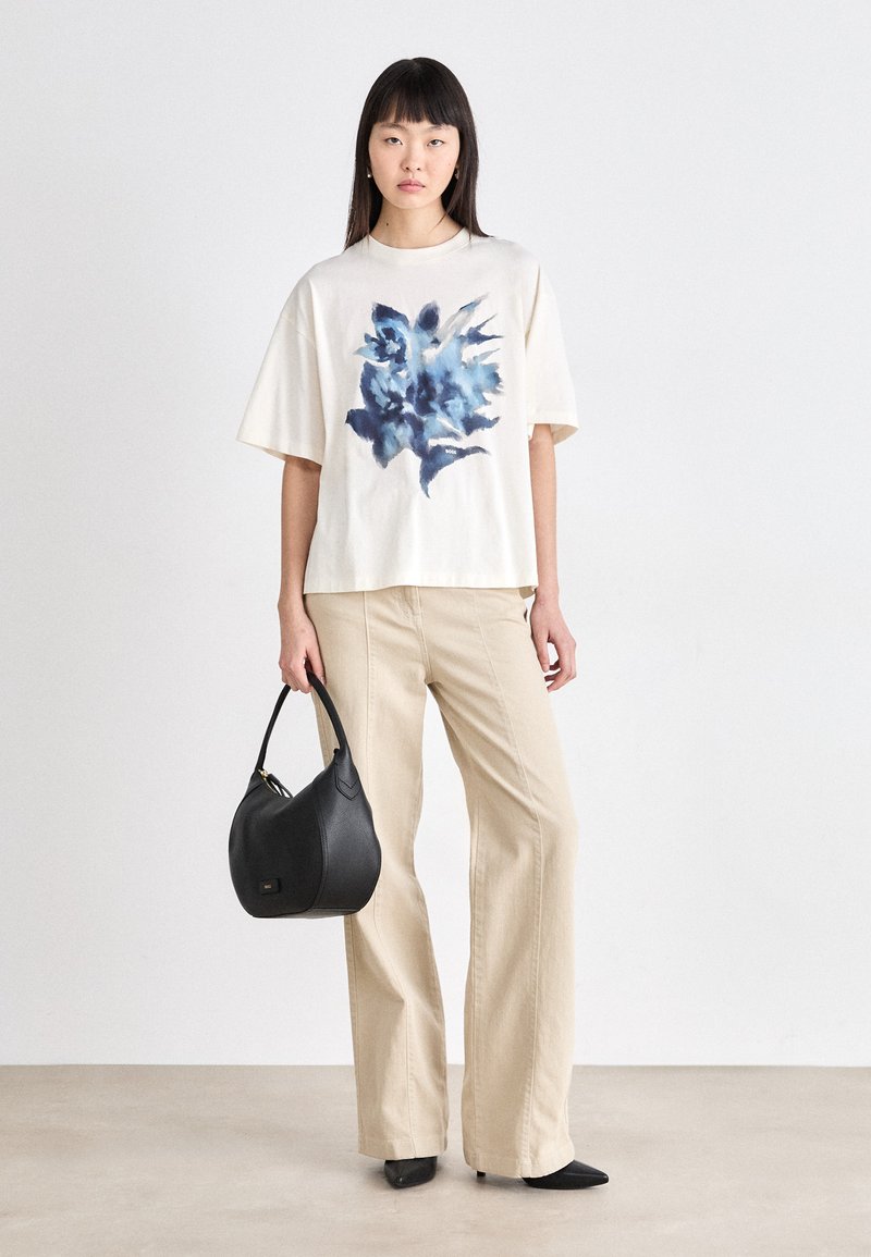 Katoenen T-shirt in ivoorkleur met een blauw bloemenmotief, gecombineerd met beige wijde broek en een zwarte leren hobotas. Eenvoudig ontwerp, losse pasvorm.