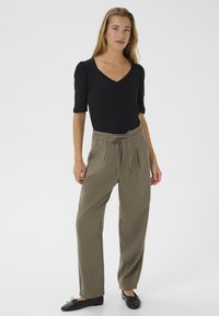 Haut noir à manches courtes avec un décolleté en V associé à un pantalon taille haute vert olive avec une ceinture à nouer. Des ballerines noires complètent la tenue.