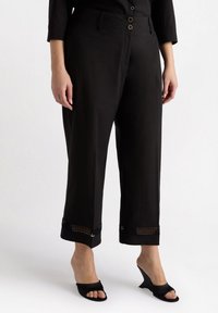 Svarta cropped byxor har en mjuk tyg, tre framknappar, sidofickor och spetsdetaljer vid fållen. Matchas med svarta klacksandaler.