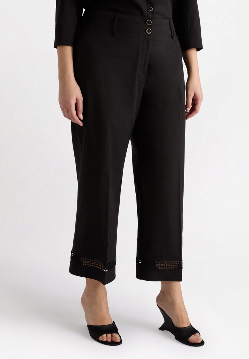 Svarta cropped byxor har en mjuk tyg, tre framknappar, sidofickor och spetsdetaljer vid fållen. Matchas med svarta klacksandaler.