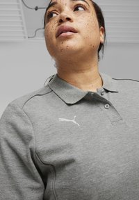 Graues Polo-Shirt mit einem Kragen, zwei Knöpfen und einem weißen Puma-Logo. Verfügt über Stickdetails entlang der Schultern.